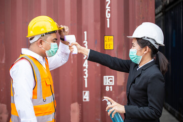 Female worker scanning fever temperature with digital thermometer to construction site staff...