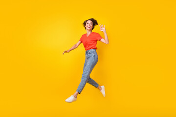 Fototapeta na wymiar Full size profile photo of hooray brunette short hairdo lady jump wave hand wear t-shirt jeans sneakers isolated on yellow background