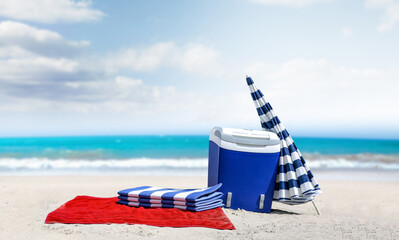 Summer background of beach with landscape of sea. Red towel with tourist fridge and beach umbrella....