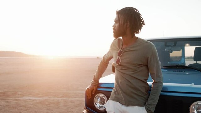The African man standing near the car in front of the sunset on the sand