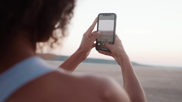The close-up view of the African female hands taking a photo of the sunset on the phone in the nature