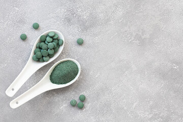 Green algae in powder and pills - chlorella, spirulina a gray background. Healthy green food supplement concept