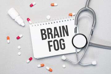 In the notebook is the text brain fog next to a stethoscope, pills and glasses.