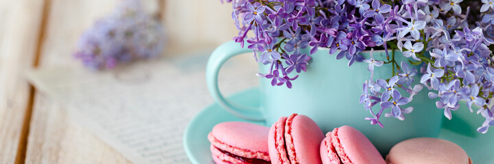 Banner with violet lilac bouquet in a blue cup and delicious french macarons. Template for birthday card, greeting for Mother's Day, Saint Valentine's day, 8 March, Women's Day. White background