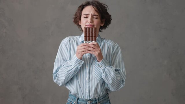 The woman with short hair holding a chocolate bar in her hands and sniffing it with pleasure in a gray studio