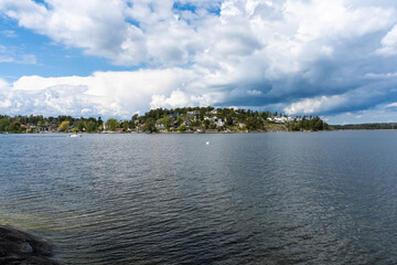 Amazing Panorama of the Baltic Sea Bay on sunny spring day. Rocky shores of Scandinavia covered with evergreen forests. Traditional Swedish wooden villas houses on the coast. Blue sky white clouds.