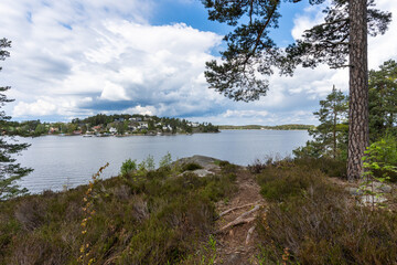 Fototapeta na wymiar Amazing Panorama of the Baltic Sea Bay on sunny spring day. Rocky shores of Scandinavia covered with evergreen forests. Traditional Swedish wooden villas houses on the coast. Blue sky white clouds.