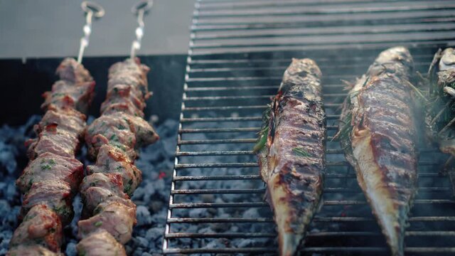 Pork meat shashlik and scomber fish cooking on barbeque grill. Smoke rising