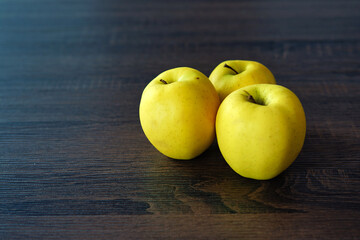 Three yellow apples on a dark table.
Three sweet apples placed close together on dark brown varnished wood. Natural products, fruit and healthy diet.