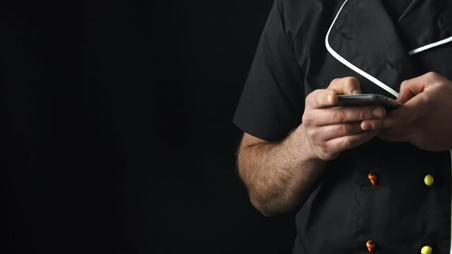 Torso of a man in a black apron using a smartphone,black background.