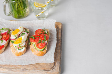 Toasted sandwiches white bread with cream cheese, vegetables: cherry tomatoes, cucumbers, eggs, parsley. Healthy vegetarian breakfast idea. Served on craft paper, light background, copy space