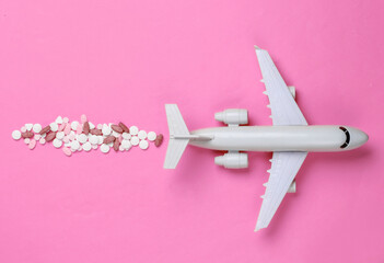 Figurine of a passenger plane with pills on pink background. Top view.