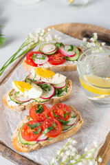 Toasted sandwiches white bread with cream cheese, vegetables: cherry tomatoes, cucumbers, eggs, parsley. Healthy vegetarian breakfast idea. Served with fresh lemon water, light background, copy space