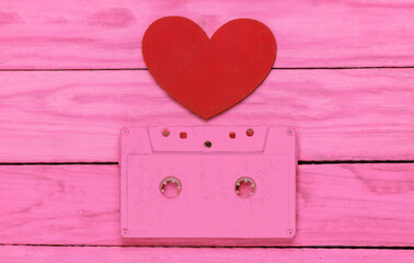 Music lover concept. Audio cassette with a heart on pink wooden background. Retro 80s. Top view.