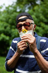 Latina american man in sunglasses and mask likes sniffing dandelion