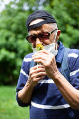 Latina american man in sunglasses and mask likes sniffing dandelion