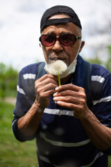Latina american man in sunglasses and mask likes sniffing dandelion