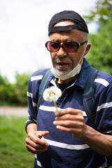 Latina american man in sunglasses and mask likes sniffing dandelion
