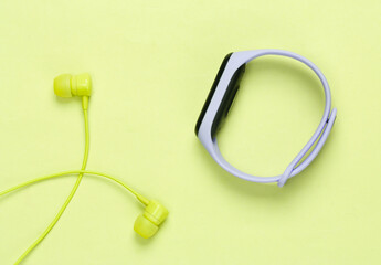 Earphones with smart bracelet on yellow pastel background. Modern gadgets. Top view