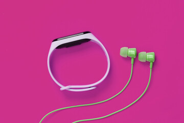 Earphones with smart bracelet on pink background. Modern gadgets. Top view