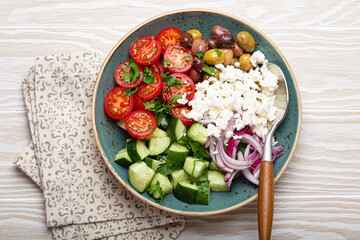 Greek mediterranean salad with tomatoes, feta cheese, cucumber, whole olives and red onion in blue ceramic plate on white wooden background from above, traditional appetizer of Greece 