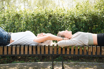Two happy women having a rest on a park bench. Girl tickling her girlfriend. Smiling female friends...