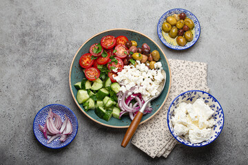 Greek mediterranean salad with tomatoes, feta cheese, cucumber, whole olives and red onion in blue ceramic plate on gray concrete background from above, traditional appetizer of Greece