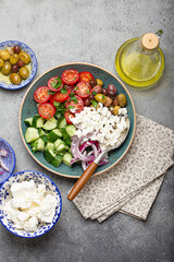 Fototapeta na wymiar Greek mediterranean salad with tomatoes, feta cheese, cucumber, whole olives and red onion in blue ceramic plate on gray concrete background from above, traditional appetizer of Greece