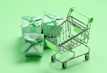 Supermarket trolley with gift boxes on green pastel background