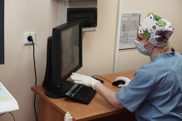 A woman radiologist behind the monitor makes an X-ray correction.