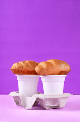 Croissant and disposable cup of coffee in carton holder against the purple background. Takeaway food and drink