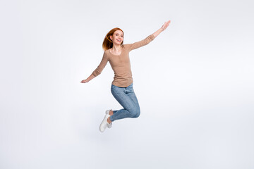 Fototapeta premium Full length photo of adorable sweet redhair woman beige shirt jumping high arms sides smiling isolated white color background
