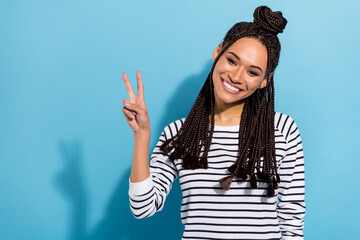 Photo portrait of smiling girl with dreadlocks top-knot wearing striped shirt showing v-sign gesture isolated pastel blue color background