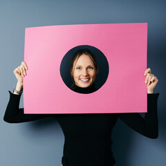 Vivacious happy blond woman framing her face with pink card