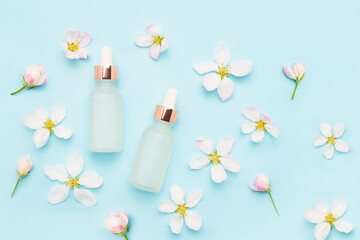 Light glass dropper bottles for cosmetic use and apple tree blossom flowers on a light blue background. SPA concept