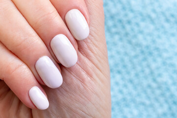 Female hand with beautiful manicure - white ivory nails on blue knitted sweater fabric background