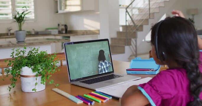 African american girl raising her hand while having video call with female teacher on laptop at home