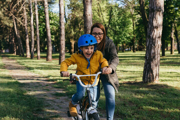 mother helps her boy to ride a bike in public park