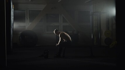 Bodybuilder sitting on a gym bench, contemplating in shadows.