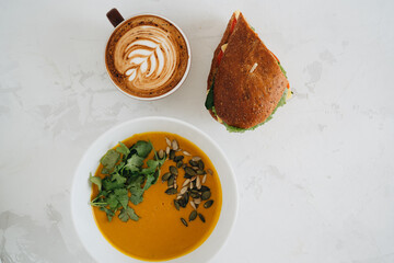 A cup of coffee, soup and panini on white table