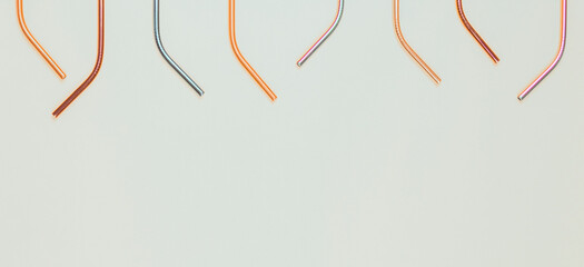 Multicolored reusable stainless steel straws on light gray background. Top view, copy space