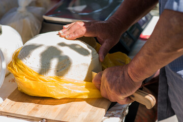 Aged farmer cutting cheese with knife on wooden board. Fresh cow's milk cheeses. Rustic hand made gourmet cheese.