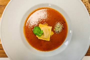 Tomato soup or gazpacho soup with Ravioli and basil on a wooden rustic table - top view.