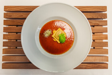 Tomato soup or gazpacho soup with Ravioli and basil on a wooden rustic table - top view.