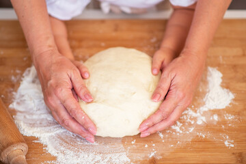 Mother and child hands prepares the dough with flour on rustic wooden table from above. Homemade pastry for bread or pizza. Bakery background.