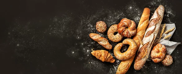 Fototapeten Brot Bakery - bread rolls, baguette, bagel, sweet bun and croissant on black background  © pinkyone