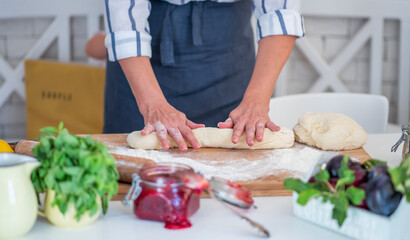 Female hands making dough. Dough with flour, eggs and other utensil, ingredients lies on white wooden table. Baking homemade process.