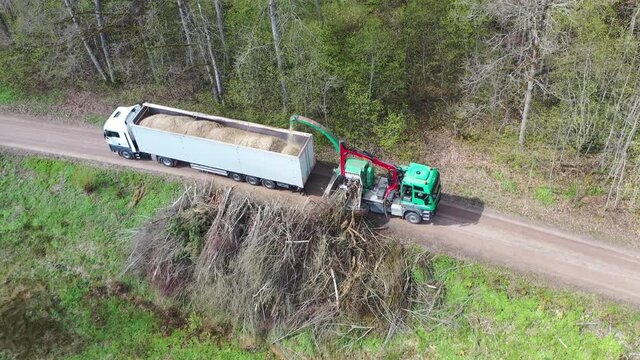 Aerial view of wood chipper blowing shredded wood into back of a truck. Forest background