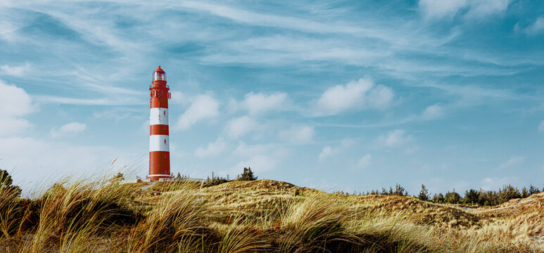 Summer evening view on lighthouse and sandy landscape around. Sandy dirt road for bikers and walkers in foreground.
