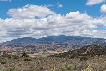 Los Padres National Forest, CA, USA - May 21, 2021: Dry mountain range in eastern part under blue cloudscape with agriculture in valley. Shrub vegetation.